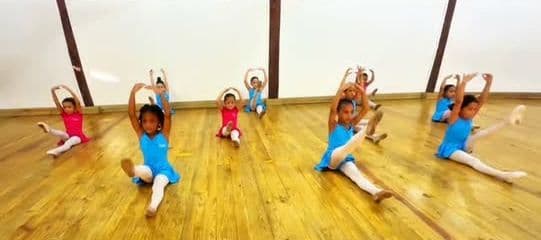 Grupo de niñas estirando en el piso de madera del salón