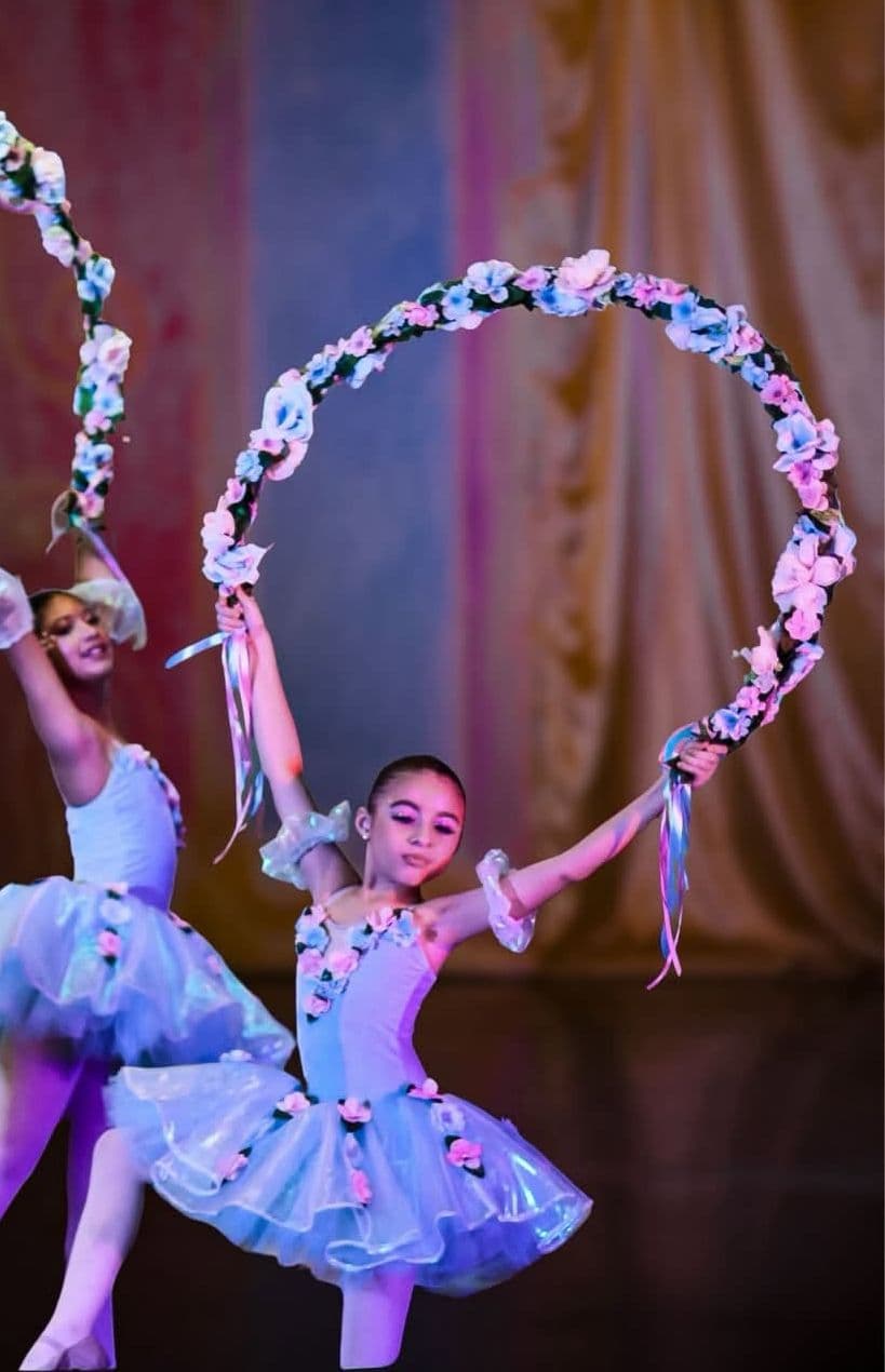 Dos alumnas en tutú lila bailan con arcos de flores en el escenario